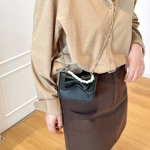 Elegant black leather mini crossbody bag with pearl handle and bow detail on model