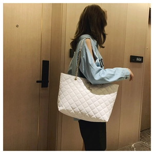 Detailed view of white quilted tote bag with gold chain strap worn by a model in a hallway