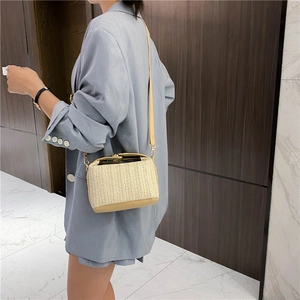 Beige straw woven crossbody bag with brown leather accents and gold buckle on model