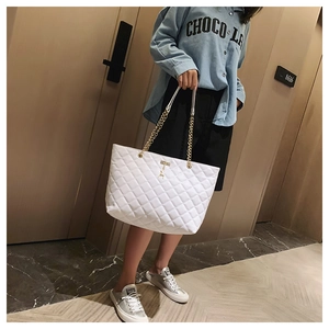 Close-up of white quilted tote bag with gold deer charm and elegant chain strap