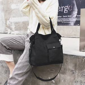 Detail of black canvas tote bag showing wide straps and front pocket with metal button