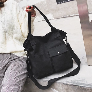 Detail of black canvas tote bag featuring dual front pockets and adjustable shoulder strap