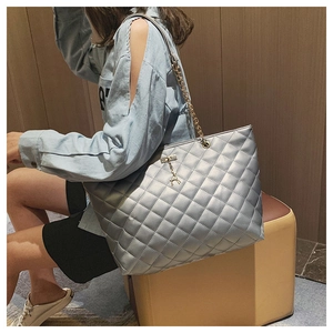 Detail of silver quilted handbag with metal chain strap and deer charm on a model