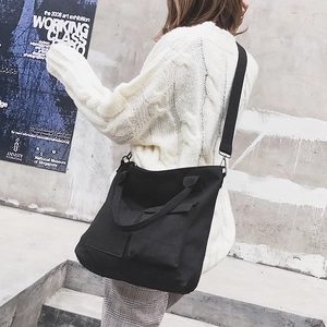 Detail of black canvas tote bag with adjustable strap worn by model in urban casual setting