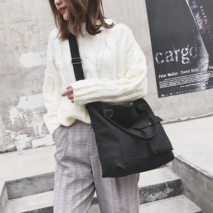 Detail of black canvas tote bag with front pocket and adjustable strap on a model
