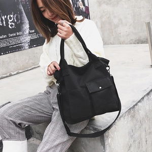 Detail of black canvas tote bag showing external pockets and adjustable crossbody strap