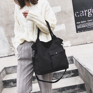 Detail of black canvas tote bag with front pockets and adjustable crossbody strap