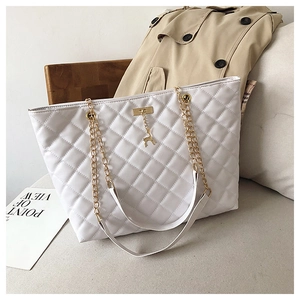 Close-up of white quilted tote bag with gold chain strap and deer pendant on grey fabric