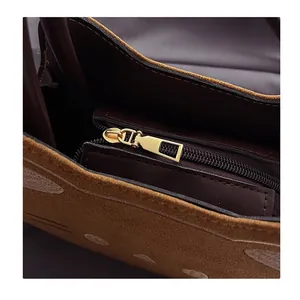 Detailaufnahme des goldenen Metallreißverschlusses und brauner Wildledertextur der Tasche
