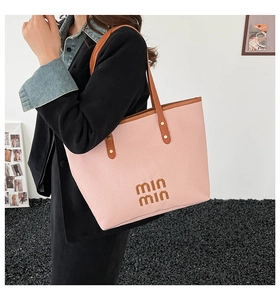 Detail view of pink leather tote bag with brown handles and stylish letter branding