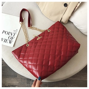 Macro shot of red quilted faux leather tote bag with golden horse charm and chain strap