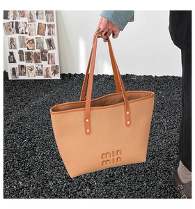 Detail view of the brown woven tote bag featuring a logo emblem and golden metal rivets