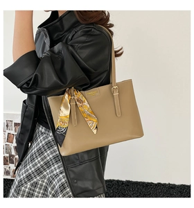 Detail of khaki leather tote bag with silk scarf and embossed fashion logo on model