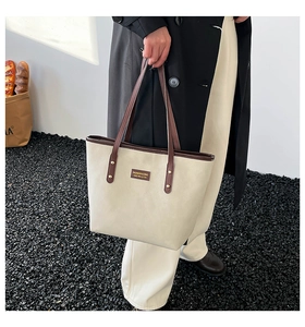 Close-up of beige tote bag with brown leather straps and fashion metal logo detail
