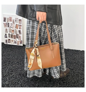 Detail of vintage brown leather tote bag with silk scarf and gold embossed logo lettering