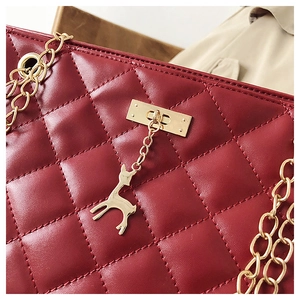 Close-up of wine red quilted leather bag with golden chain and deer charm detail