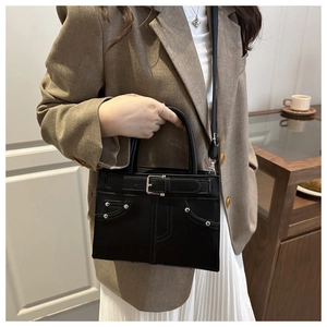 Detail of a black leather crossbody bag with metal rivets on a stylish woman