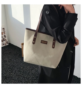 Detail of canvas tote bag with brown leather trim and metallic rivet fasteners