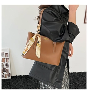 Detail of a brown leather tote bag featuring a decorative yellow geometric print silk scarf