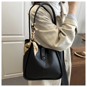 Detail of black matte leather shoulder bag featuring decorative scarf and buckle closure