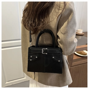 Detailed view of black leather shoulder bag with silver buckles and rivets worn by model
