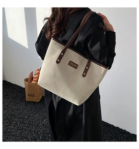 Detail of canvas tote bag with brown leather straps and fashion label on a model