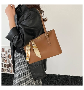 Close-up of brown leather tote bag with decorative silk scarf and adjustable strap
