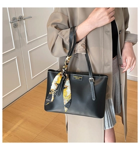 Detail of black leather tote bag with gold logo plate and decorative silk scarf