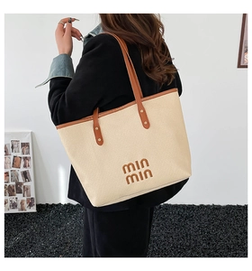 Detail of beige woven tote bag with brown leather handles and brand logo lettering