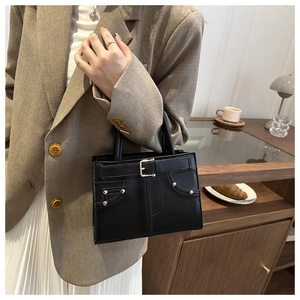Detail of black glossy leather handbag with belt buckle and metallic studs in a lifestyle setting