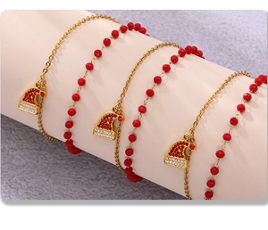 Dettaglio dei ciondoli a cappello di Babbo Natale con perle rosse su bracciale dorato