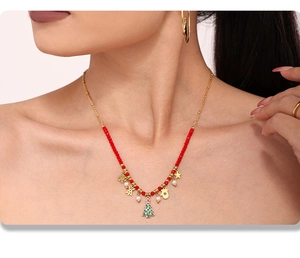 Detailed view of gold Christmas necklace with festive charms and red beads on model