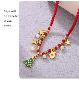 Detail of Christmas necklace with enamel tree, gold snowflakes, and red beads