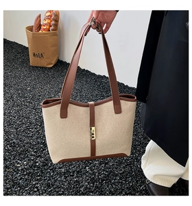 Close-up of contrast beige canvas tote bag with brown leather handles and gold lock