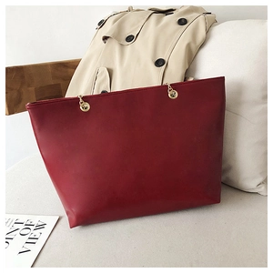 Detail of dark burgundy quilted tote bag with golden metal rings and leather texture