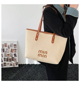 Detail of woven beige tote bag with brown leather handles and classic brand logo lettering