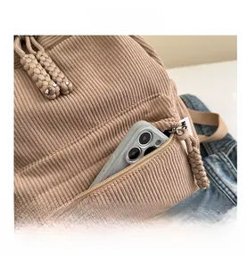 Detail view of khaki corduroy backpack featuring woven rope zipper and front pocket storage