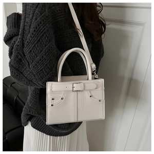 Detail of cream white leather handbag with strap and buckle accent on female model
