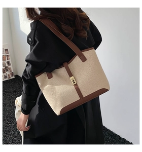 Detail of canvas tote bag showing contrast leather trim and golden metal turn-lock closure