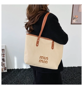 Close-up of beige woven tote bag with brown leather handles and brand embroidery