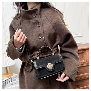 Detail of black crossbody bag with golden flower clasp and woven handle on wool coat