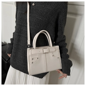 Close-up of minimalist cream leather crossbody bag with metal buckle and shoulder strap