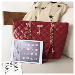 Detail of red quilted tote bag with gold deer charm and chain strap next to a tablet