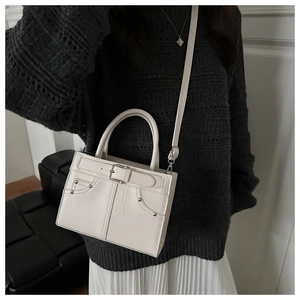 Chic cream square crossbody bag styled with a grey sweater and white pleated skirt