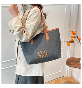 Detail of dark gray woven tote bag with brown leather handles and min min embroidery