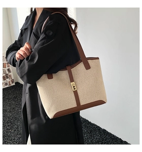 Detail of canvas tote bag with brown leather trim and metal lock on model