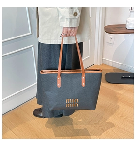 Detail of dark grey woven tote bag with brown leather handles and gold logo