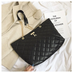 Detail of black quilted tote bag with golden deer pendant on elegant white bedding