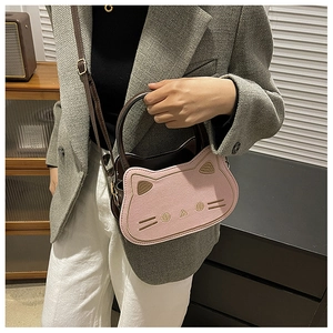 Detail view of pink cat handbag with leather handles worn by a model in a cozy room