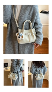 Detail of minimalist cream handbag featuring belt buckle decor and plush dog charm